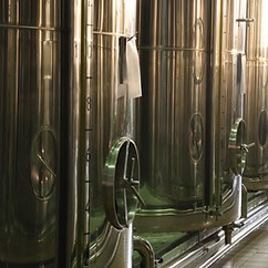 Filas de grandes tanques de fermentación de acero inoxidable en una cervecería o instalación industrial, que recuerdan el meticuloso proceso utilizado en la producción de aceite de oliva andaluz.